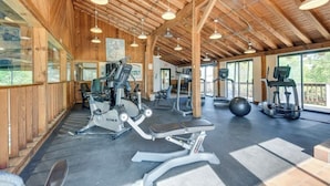 Un gimnasio con diverso equipo de ejercicio, vigas de madera en el techo y ventanas amplias.