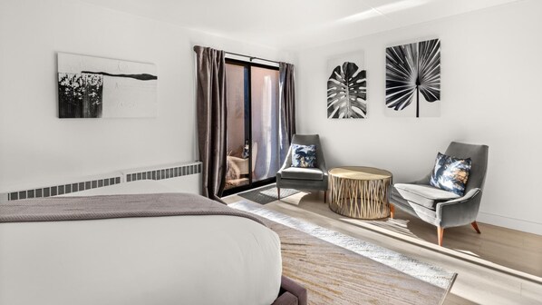 Una habitación de hotel moderna con una cama grande, dos sillones, una mesita redonda y arte abstracto en la pared.