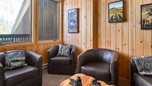 A cozy room with wooden paneled walls, two leather sofas with patterned cushions, a wooden coffee table with bear figurines, and framed pictures on the walls. - Peaceful townhome in sought-after Stowe location (Stowe)