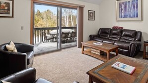 A living room with a leather sofa, a wooden coffee table, and a sliding glass door leading to a balcony with outdoor furniture. - Peaceful townhome in sought-after Stowe location (Stowe)