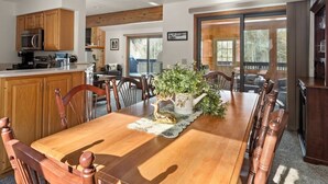A spacious dining area with a wooden table and chairs, a kitchen with wooden cabinets, and a view through large sliding glass doors. - Peaceful townhome in sought-after Stowe location (Stowe)