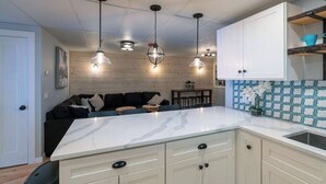 A modern kitchen with a marble countertop, white cabinetry, and pendant lighting. - Location! This Stunning 2 Bedroom on Main Street. (Stowe)
