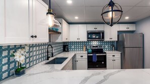 A modern kitchen with white cabinets, a stainless steel refrigerator, a microwave, and a stove. - Location! This Stunning 2 Bedroom on Main Street. (Stowe)