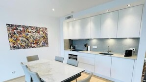 Uma cozinha moderna com armários brancos, bancada de mármore e um espaço de jantar com mesa e cadeiras.