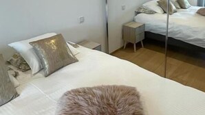 Quarto com uma cama grande, uma mesinha de cabeceira pequena, um tapete macio e um espelho.