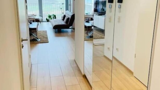 Um apartamento moderno com piso de madeira, sala de estar com sofá e televisão, e cozinha com armários e micro-ondas.