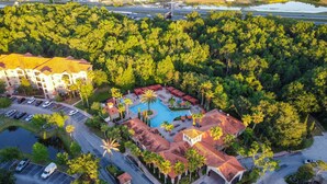 An aerial view of a resort with a swimming pool, a parking lot, and surrounding greenery. - Florida Vacation Condo - No Resort Fees. Gated Resort, Gym, Pool, Hot Tub (Davenport)