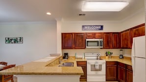 A modern kitchen with wooden cabinets, a granite countertop, a built-in oven, and a microwave. - Florida Vacation Condo - No Resort Fees. Gated Resort, Gym, Pool, Hot Tub (Davenport)