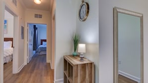 A hallway with wooden flooring, a bedside table with a lamp, a mirror, and a clock on the wall. - Florida Vacation Condo - No Resort Fees. Gated Resort, Gym, Pool, Hot Tub (Davenport)