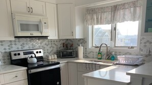 A modern kitchen with white cabinets, a microwave, a stove, a sink, and a window with a view of houses.