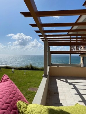 A covered outdoor area with a view of the sea, a grassy lawn, and a tiled floor. - Sunset House With Seaview Terrace by Vacationy (Alcobaça)