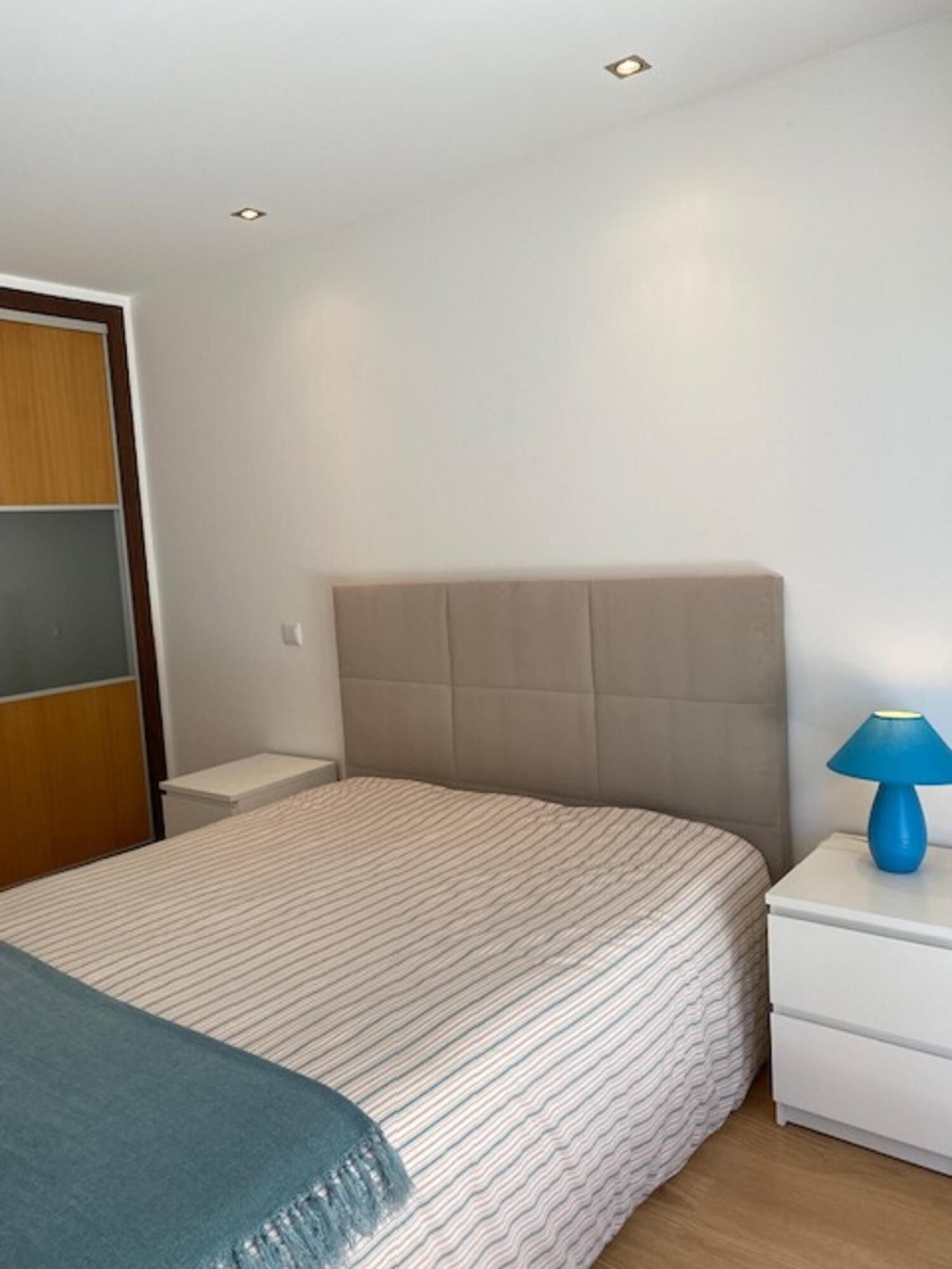 Quarto com cama, mesa de cabeceira, luminária e guarda-roupa.