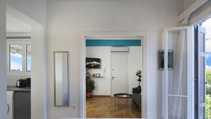 A modern bedroom with a large bed, a view of the city through a window, a kitchen area, and a dining table with chairs. - AgiouOrous10  ·  Acropolis view top floor apartmen (Athens)