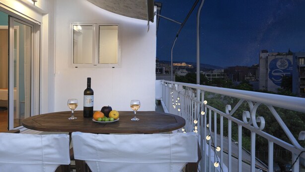 A balcony with a table set for two, featuring a bottle of wine, glasses, and fruit. - AgiouOrous10  ·  Acropolis view top floor apartmen (Athens)