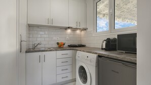 A modern kitchen with white cabinets, a built-in oven, a washing machine, and a window with a view of the sky. - AgiouOrous10  ·  Acropolis view top floor apartmen (Athens)