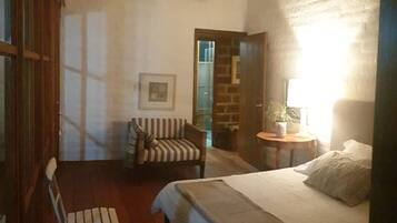 A bedroom with a bed, a chair, a small table with a lamp, and a picture on the wall.