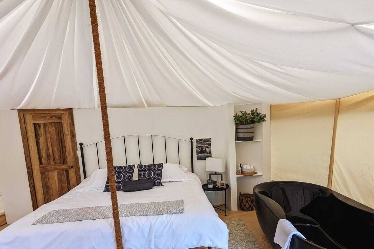 Quarto com tenda, cama, mesa de cabeceira, luminária e cadeira.