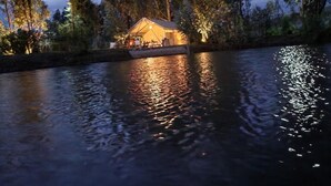 A lakeside cabin with a deck and outdoor seating area, surrounded by trees and reflecting on the water. - Palumbo Glamping & Villas (Cangahua)