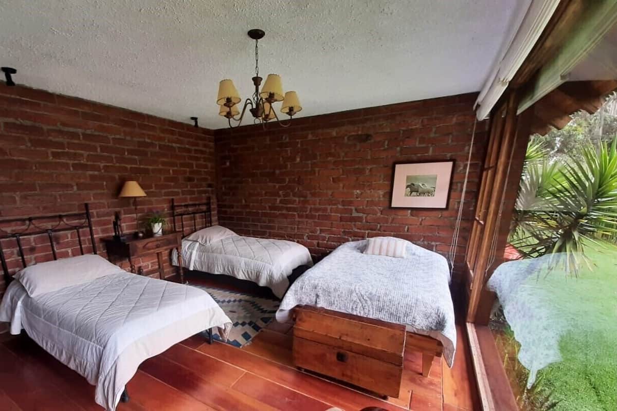 Um quarto com duas camas, um baú de madeira, um candelabro e uma parede de tijolos.