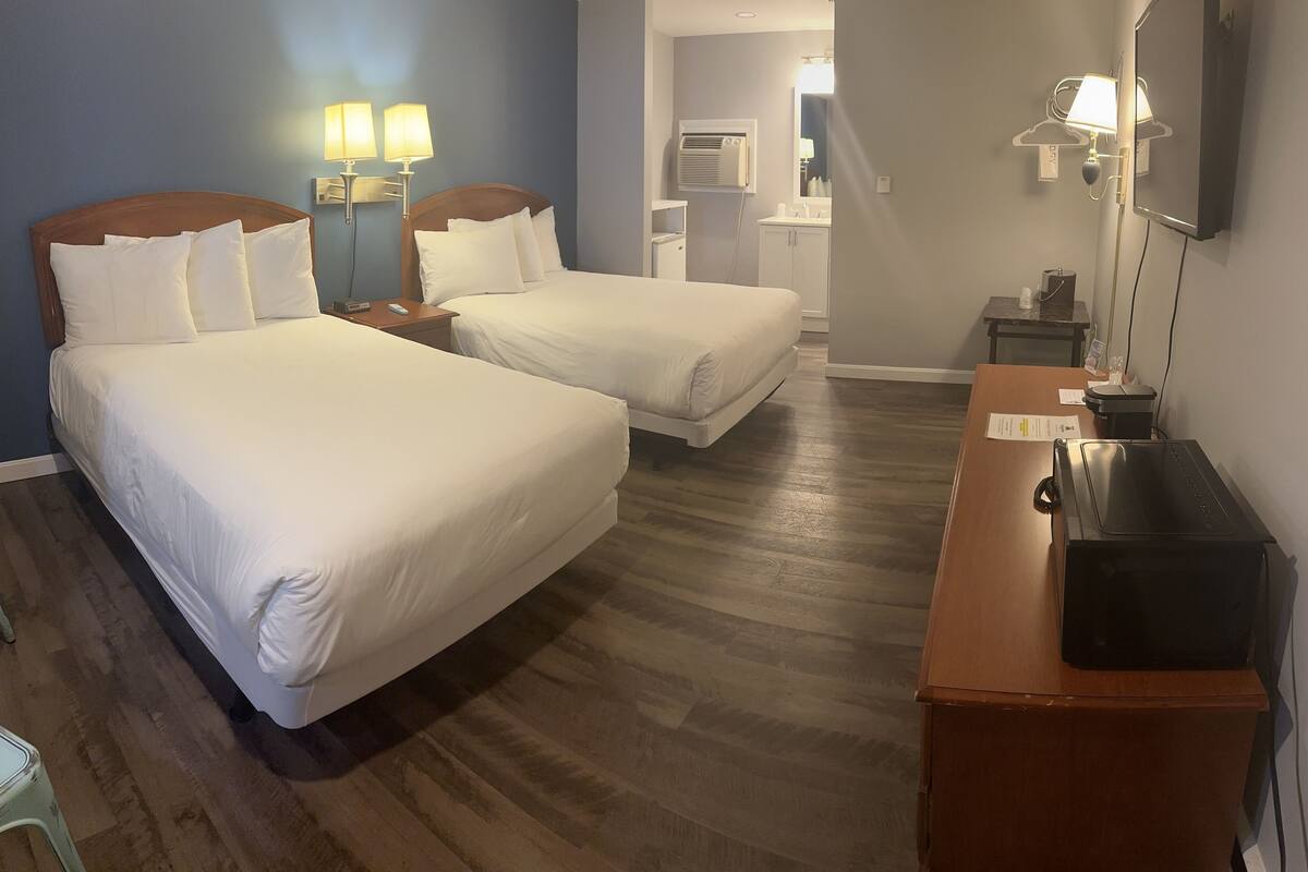Ein Hotelzimmer mit zwei Betten, einem Schreibtisch, einem Spiegel und einem kleinen Tisch.