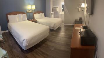 Quarto de hotel com duas camas, uma escrivaninha, um espelho e uma pequena mesa.