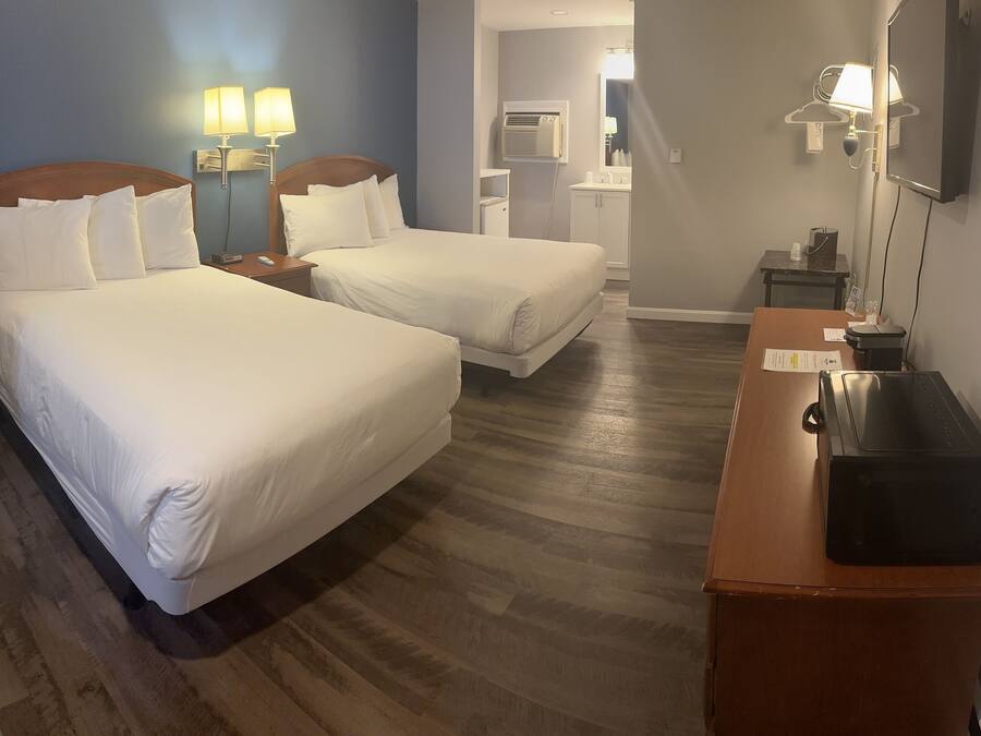 Quarto de hotel com duas camas, uma escrivaninha, um espelho e uma pequena mesa.