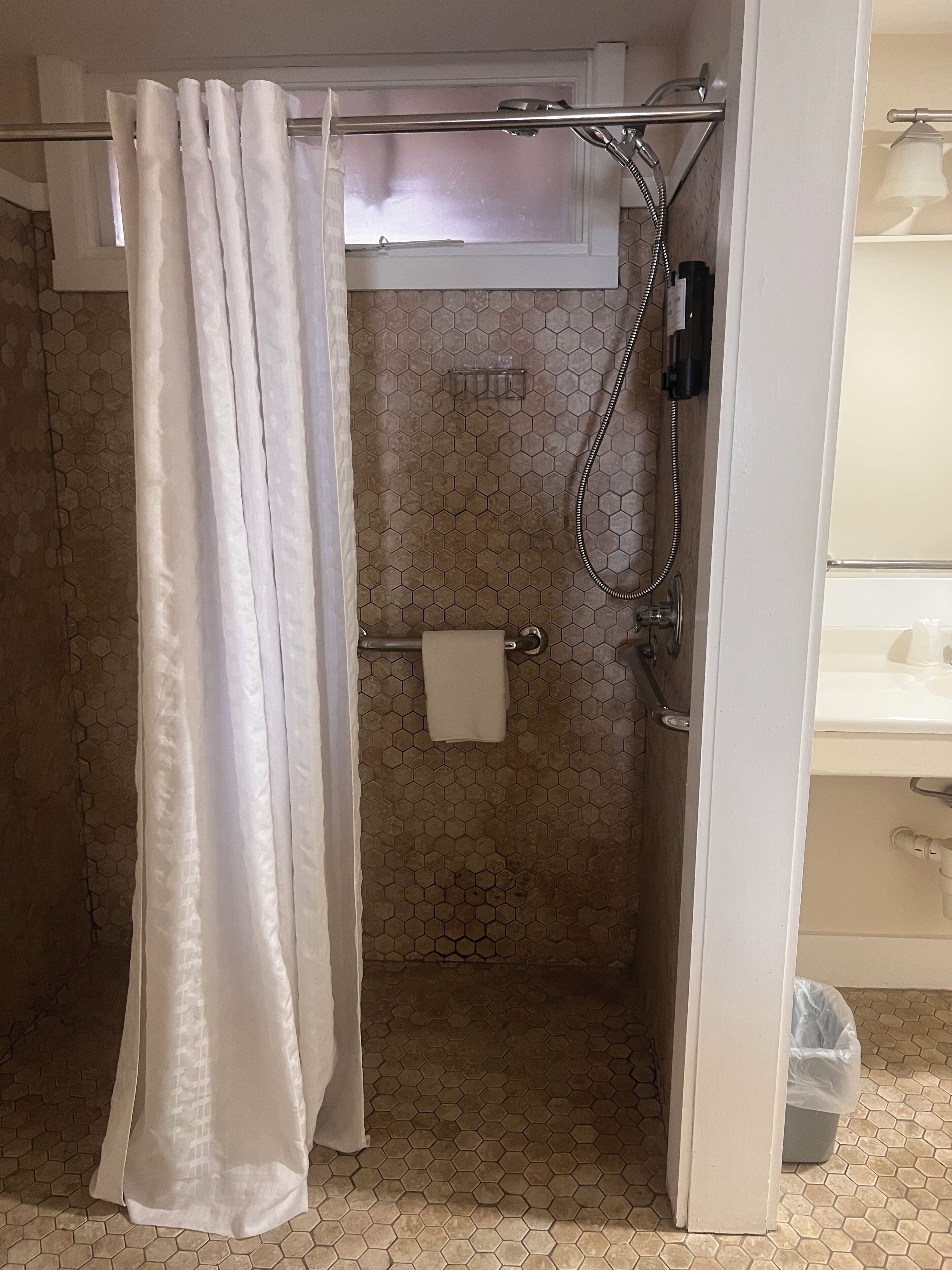 A shower area with a white shower curtain, a towel rack with a towel, and a showerhead.