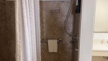 A shower area with a white shower curtain, a towel rack with a towel, and a showerhead.