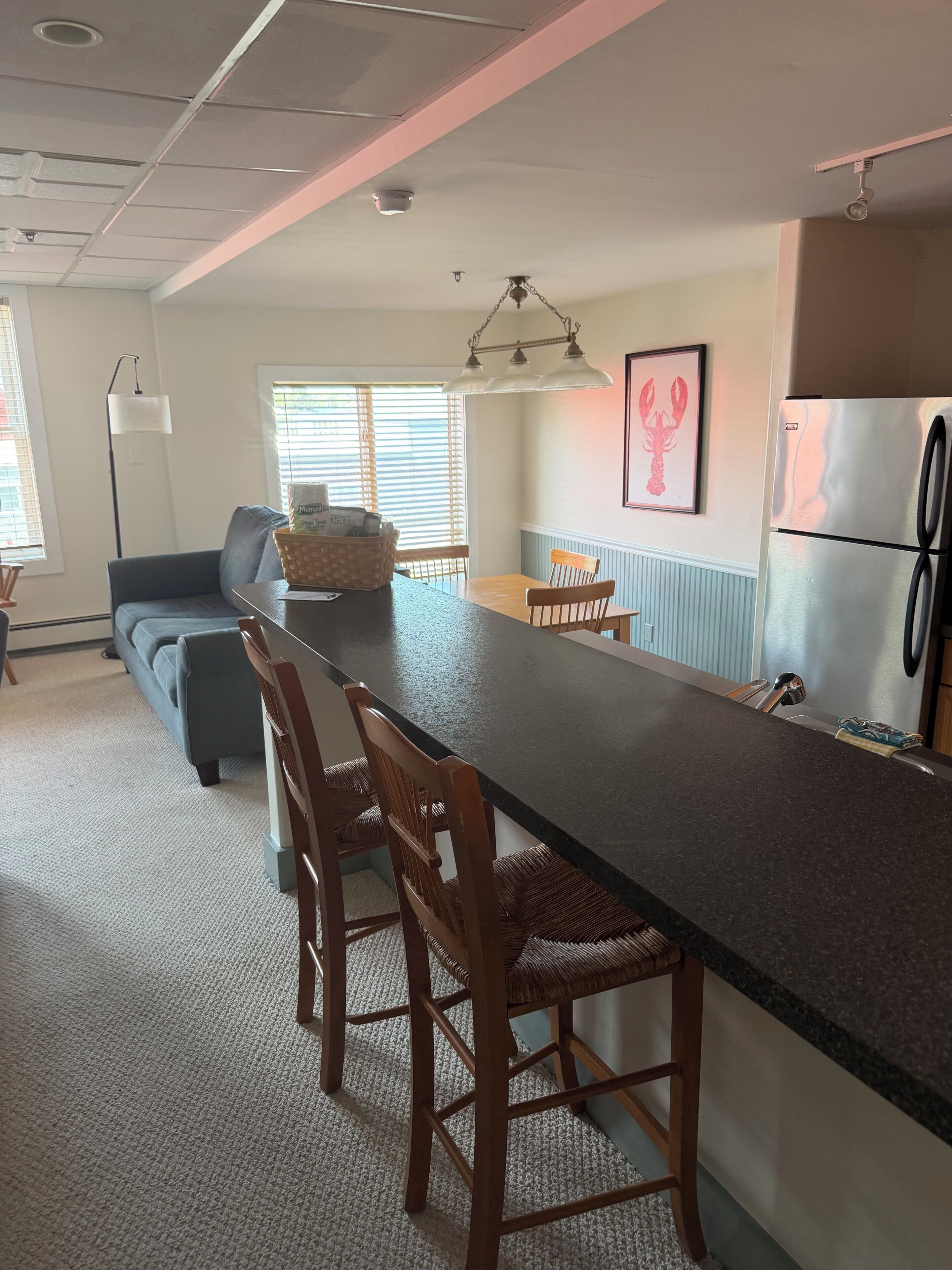 A kitchen with a central island, wooden chairs, a refrigerator, and a dining table.