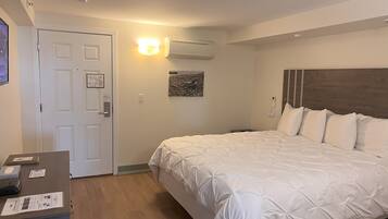 A hotel room with a large bed, a desk with paperwork, an air conditioning unit, and a door with a light switch.