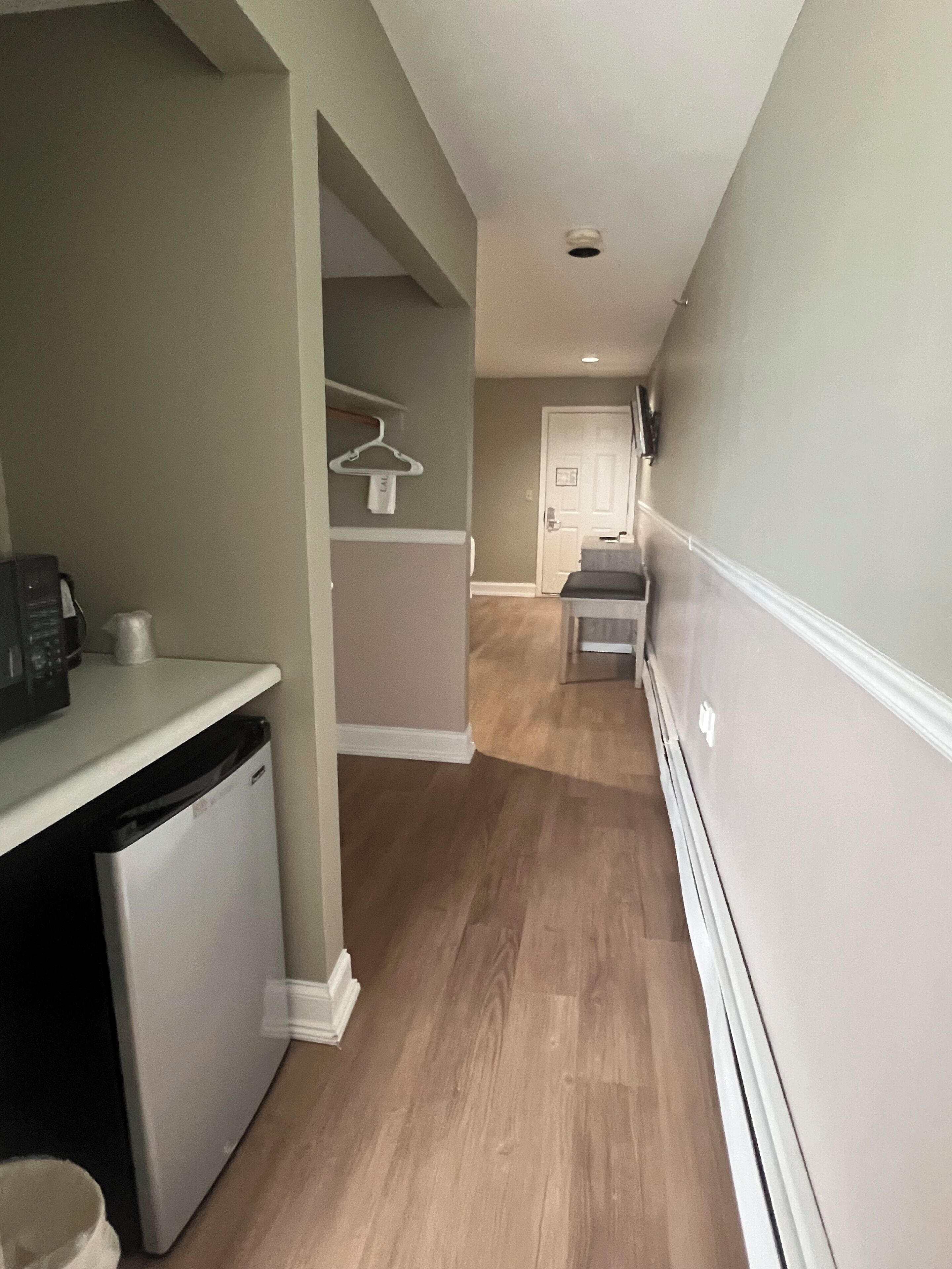 A narrow hallway with a kitchen area on the left, a door at the end, and a white wall on the right.