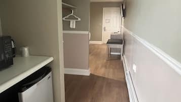 A narrow hallway with a kitchen area on the left, a door at the end, and a white wall on the right.