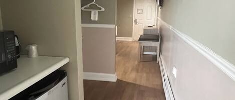 A narrow hallway with a kitchen area on the left, a door at the end, and a white wall on the right.