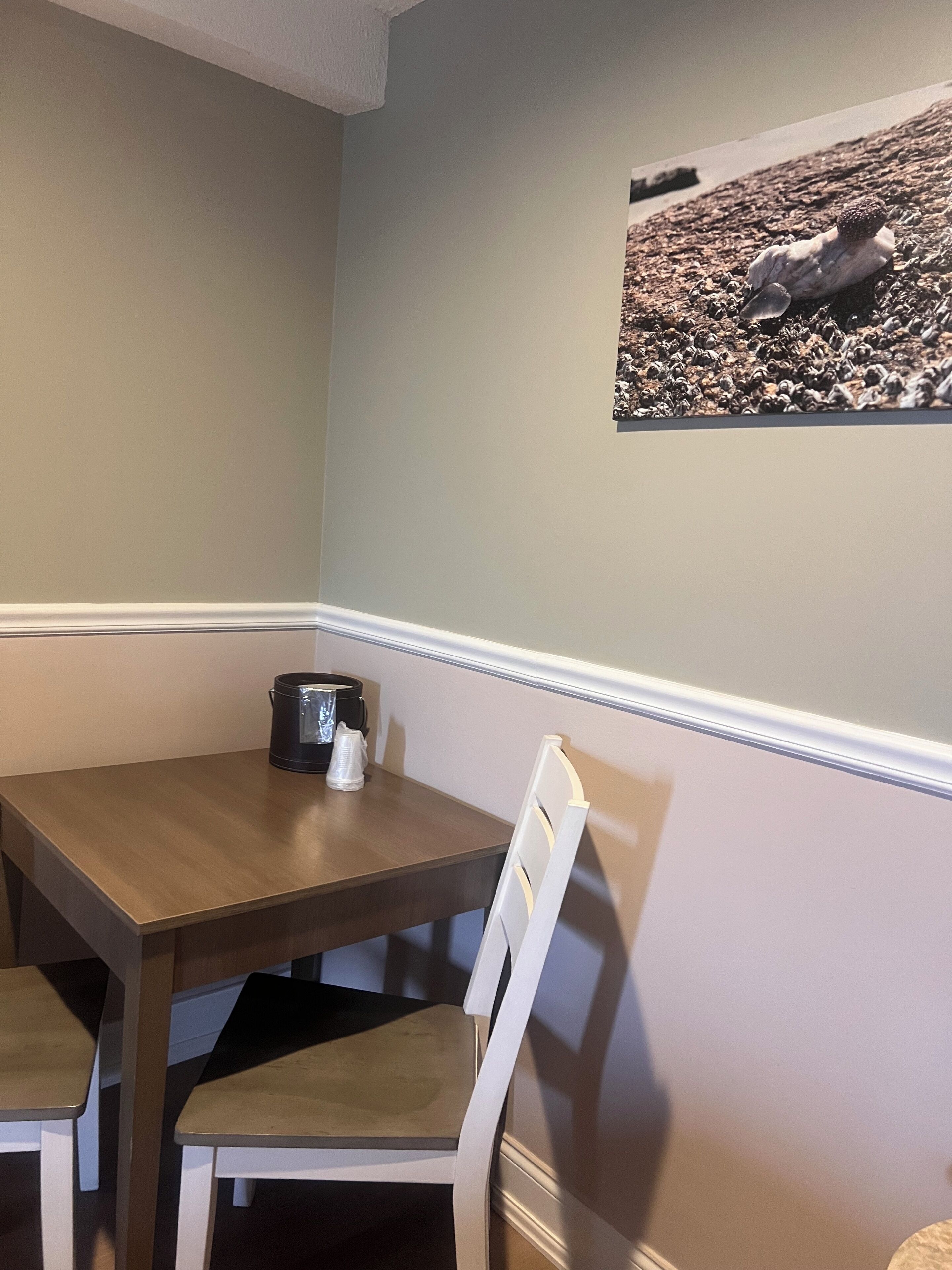 A dining area with a table and chairs, a coffee maker, and a framed picture on the wall.
