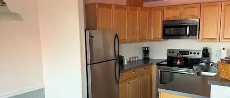 A compact kitchen with wooden cabinets, a stainless steel refrigerator, a microwave, and a stove.