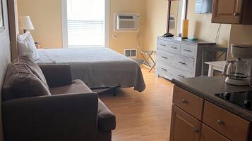 A bedroom with a bed, a sofa, a dresser, and a kitchenette.
