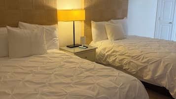A hotel room with two beds, a nightstand, and a lamp.