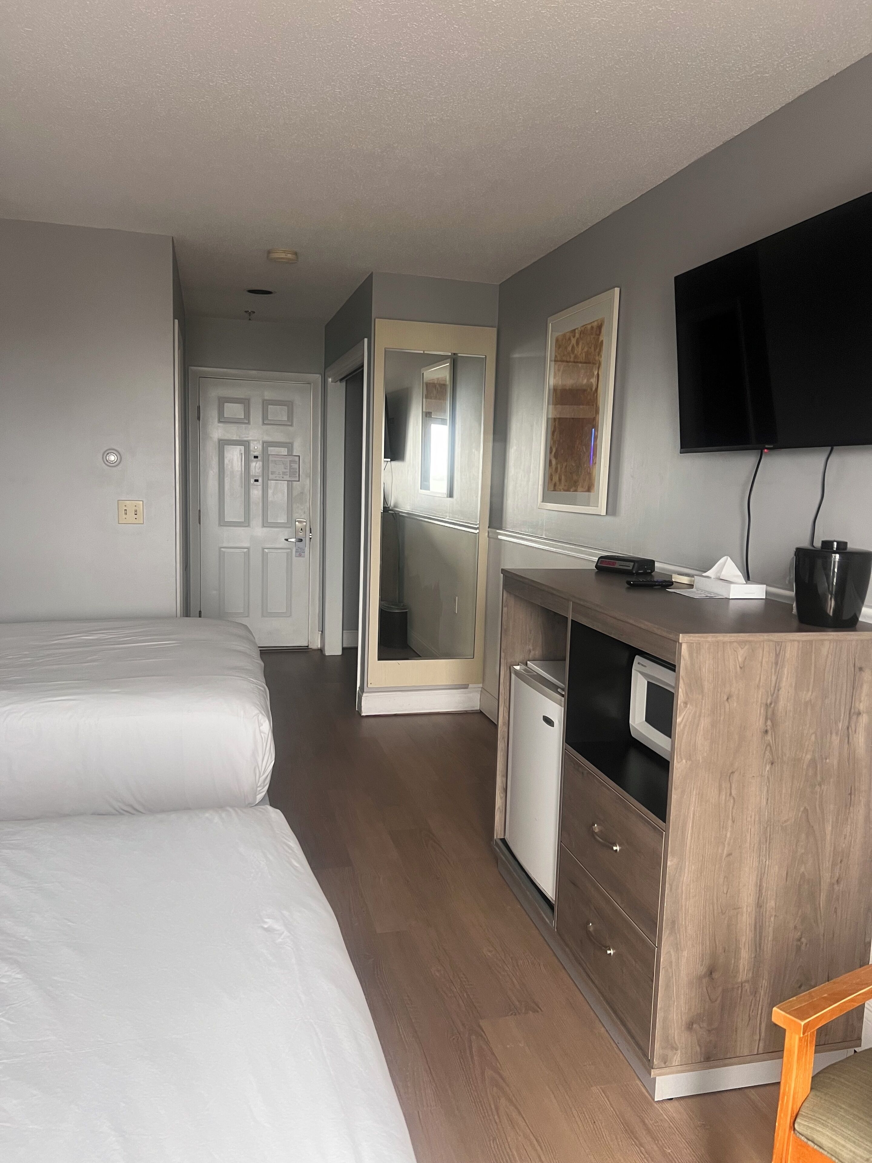 A hotel room with two beds, a wooden desk, a television, and a small refrigerator.