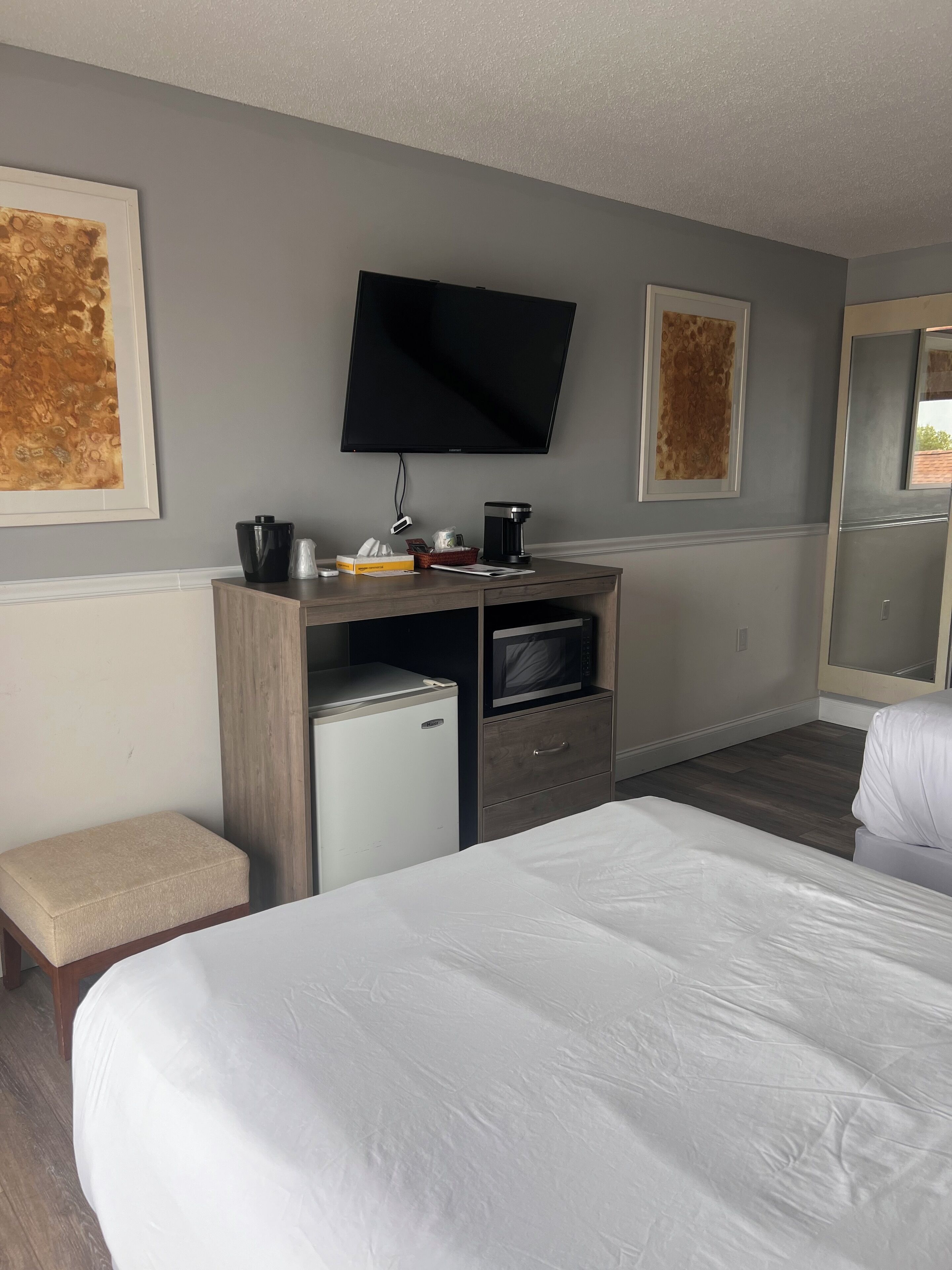 A hotel room with a bed, a desk with a coffee maker, a TV, and artwork on the walls.