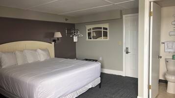 Ett hotellrum med en stor säng, ett nattduksbord, en vägglampa, ett fönster med utsikt och en dörr som leder till badrummet.