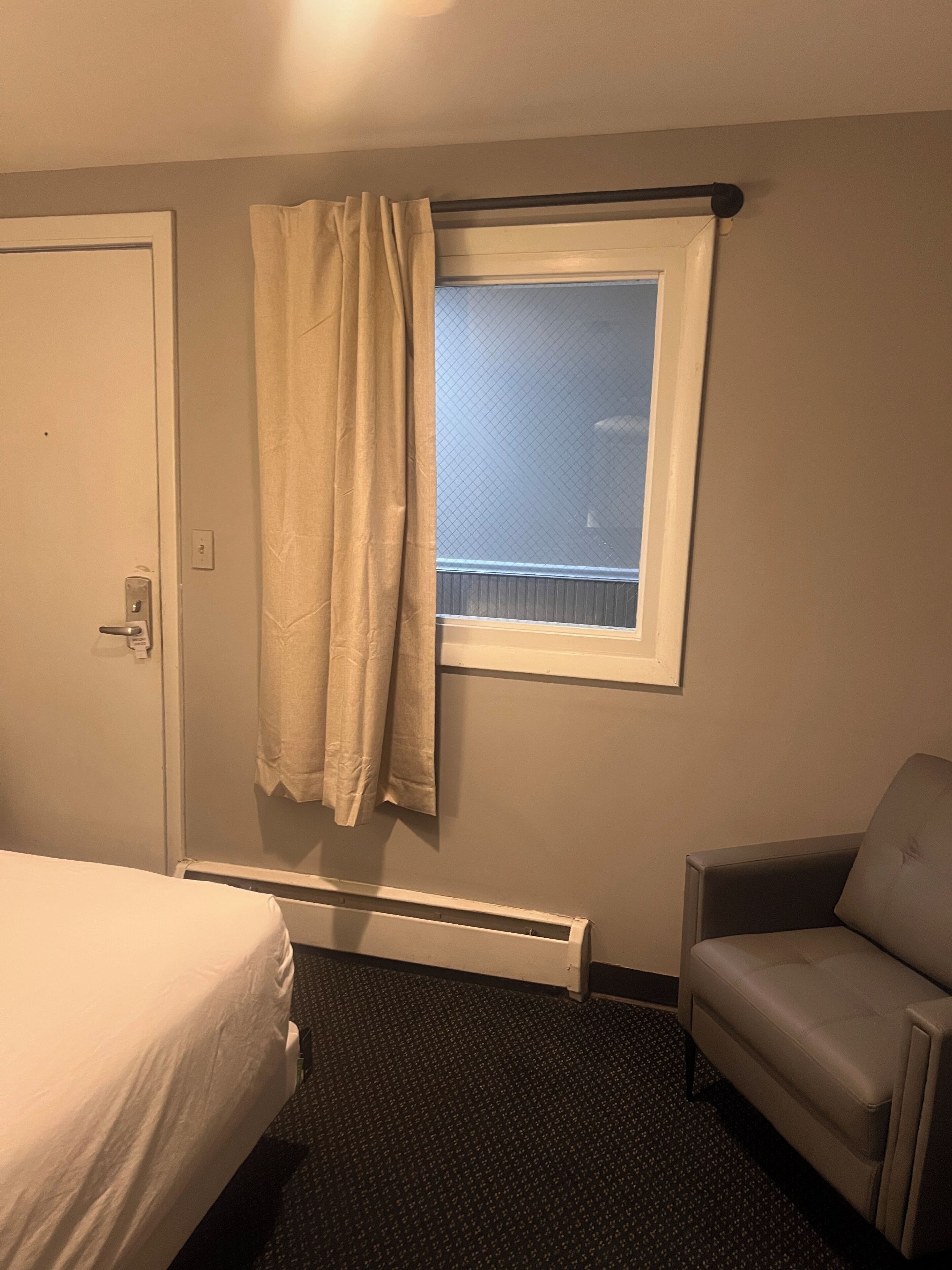 A hotel room with a bed, a chair, a window with a view, and a radiator.