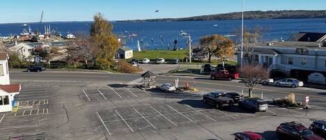 A parking lot with several cars, a red truck, and a view of a harbor with boats and a crane.