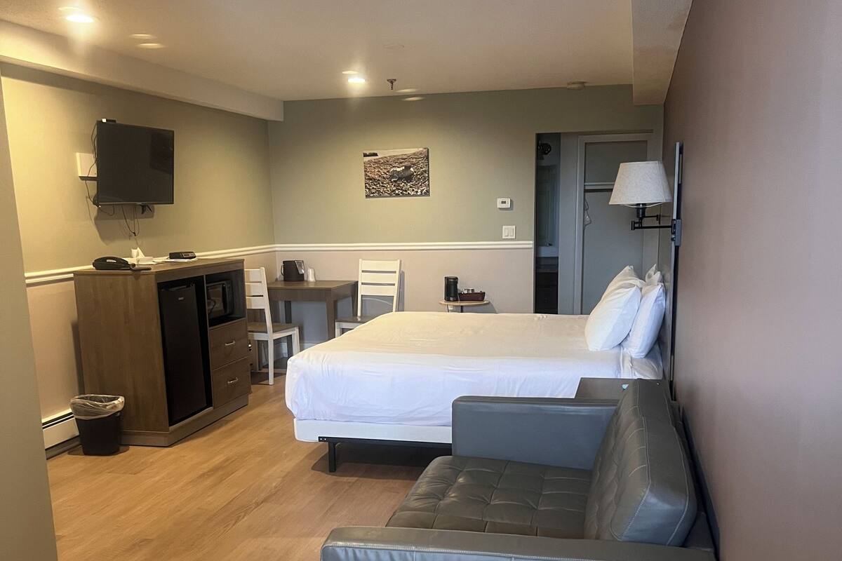 Ein Hotelzimmer mit einem Bett, einem Sofa, einem Schreibtisch mit Computer, einem an der Wand montierten Fernseher und einem kleinen Tisch mit Lampe.