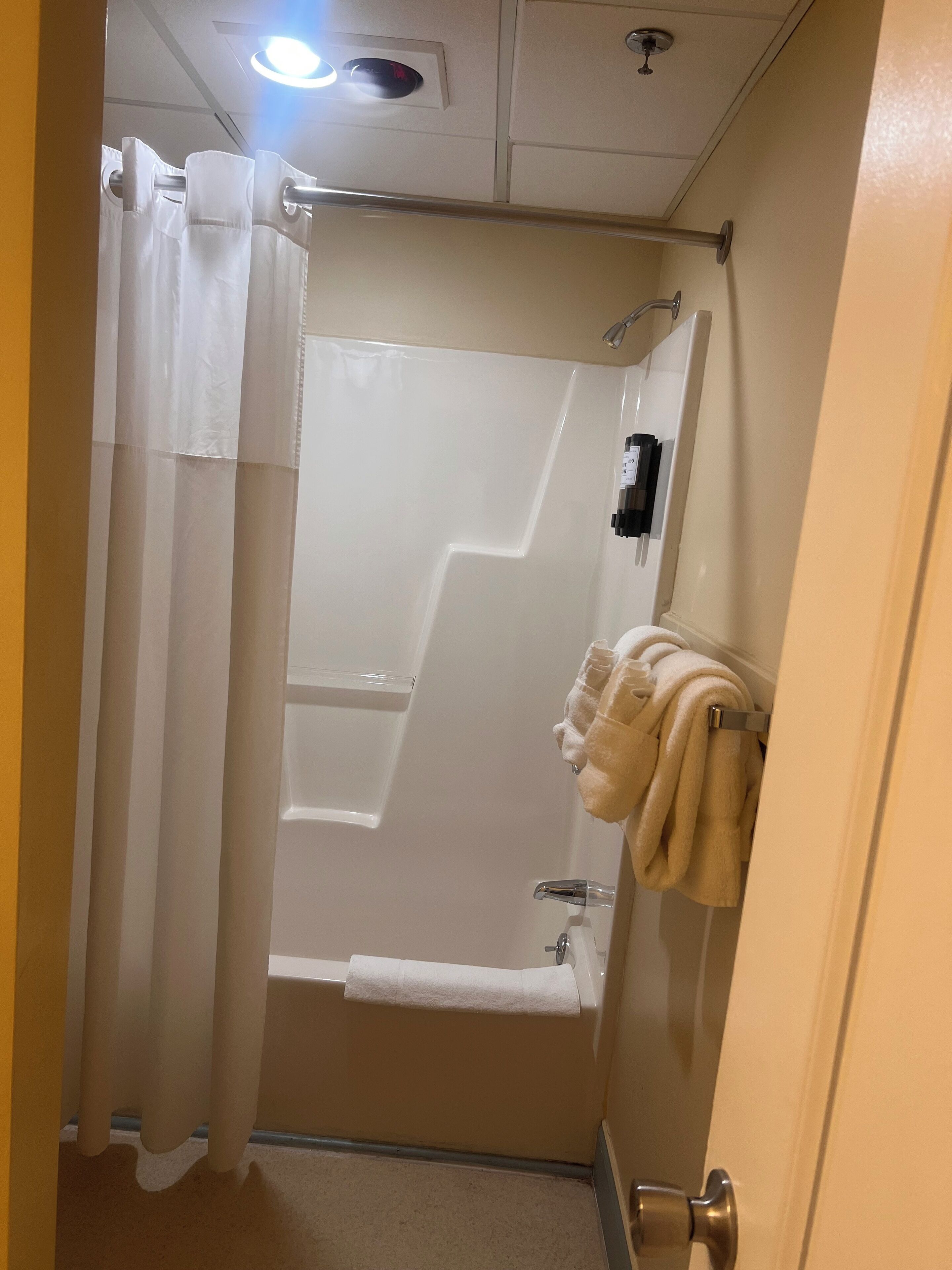 A bathroom with a shower, a towel rack with towels, and a toilet paper holder.