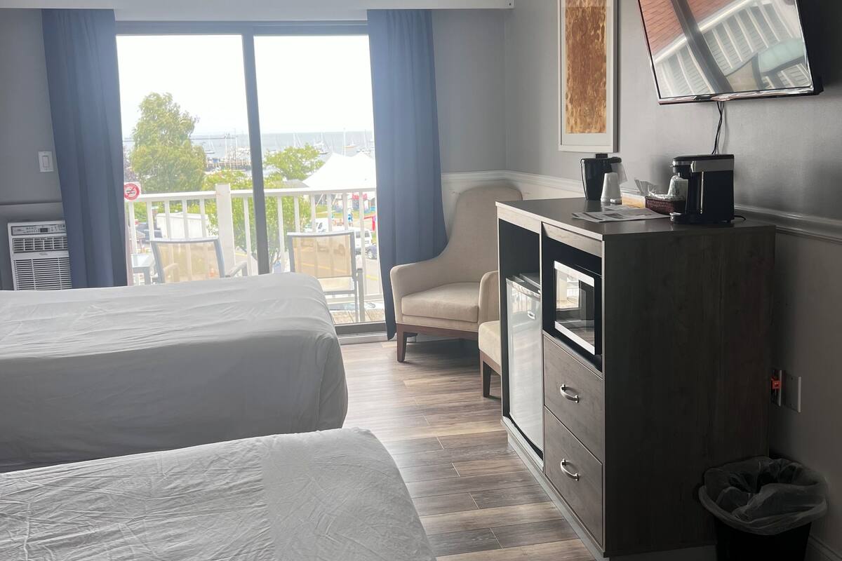 Ein Hotelzimmer mit zwei Betten, einem Schreibtisch mit Kaffeemaschine, einem Fernseher und einem Balkon mit Blick.