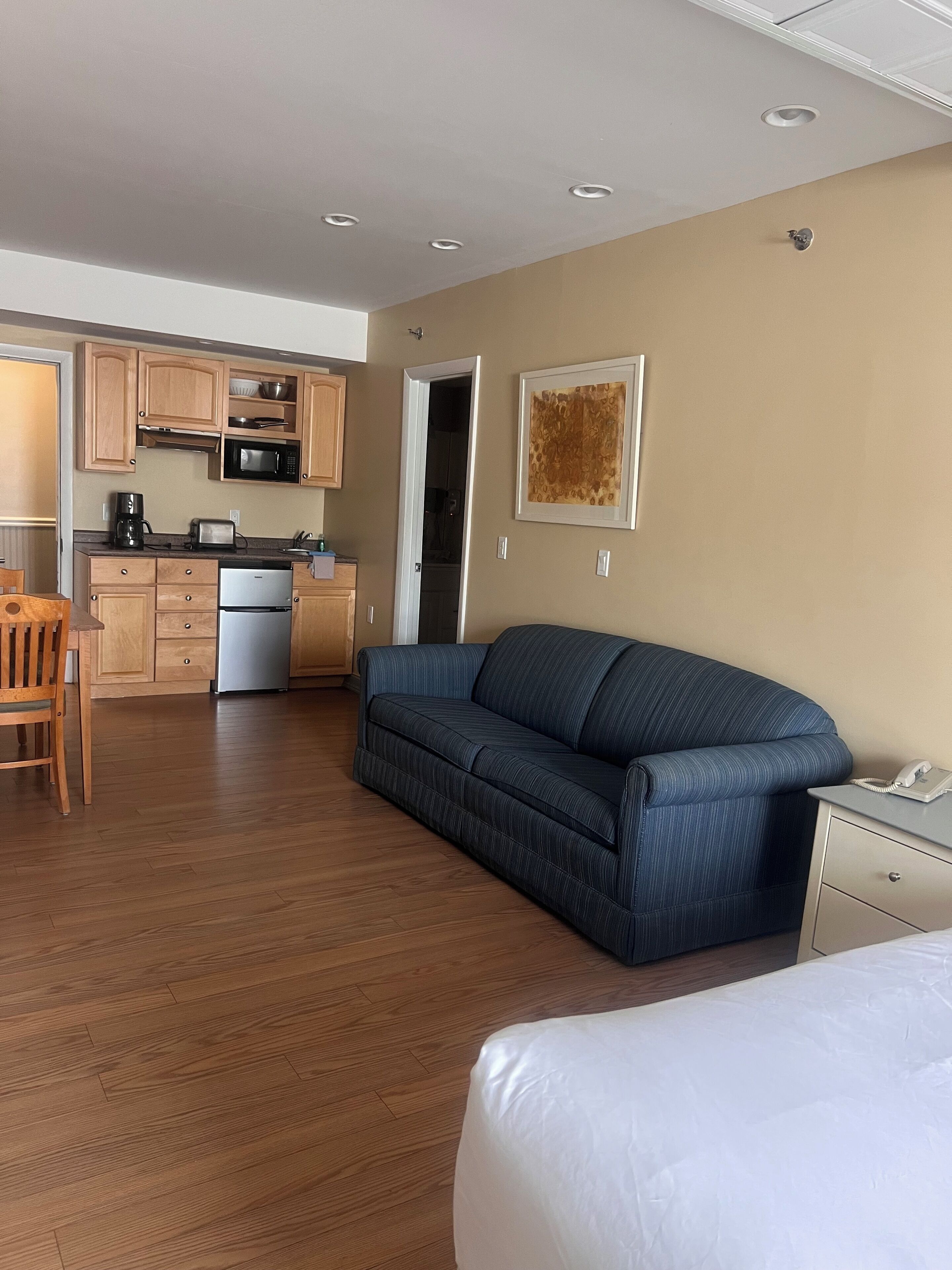 Une chambre d’hôtel avec un plancher en bois, un canapé bleu, un lit, un bureau avec un téléphone et une kitchenette dotée de meubles en bois et d’un four à micro-ondes.