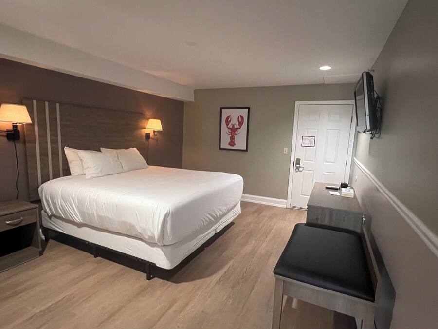 A hotel room with a large bed, bedside lamps, a desk with a chair, a door, and a wall-mounted TV.