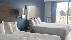 A hotel room with two beds, a nightstand, a lamp, and a view of the outside. - Trade Winds on the Bay (Rockland)