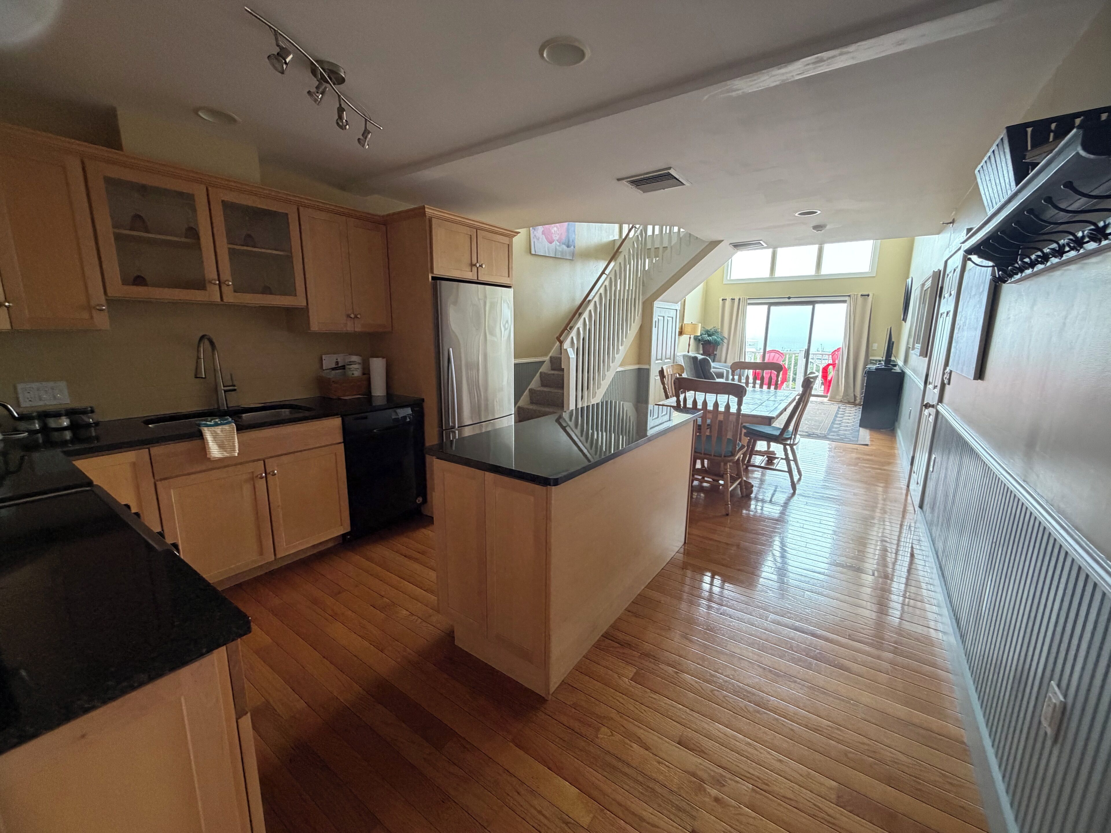 Una cocina con armarios de madera, un refrigerador de acero inoxidable y un comedor con una escalera que sube a un nivel superior.