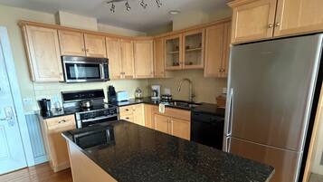 A modern kitchen with wooden cabinets, a granite countertop, stainless steel appliances, and a central island.